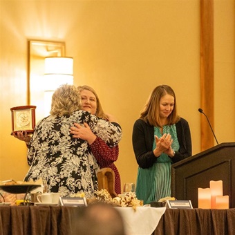 Two women hugging at an awards banquet in celebration of receiving an award.