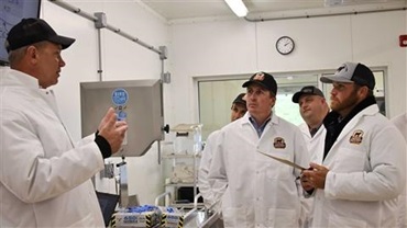 Men in white smocks listening intently to speaker in a meat lab