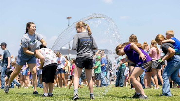 A lot of kids playing with water toys on a green grass lawn.