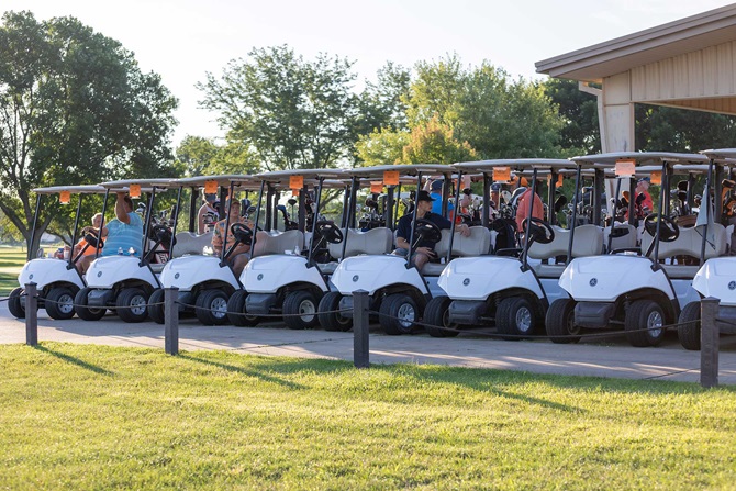 Line of golf carts with players seated waiting for tee off time.