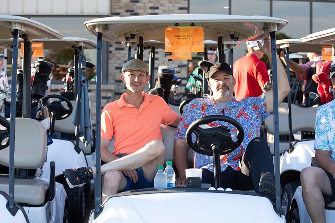 Two men sitting casually on golf cart smiling.