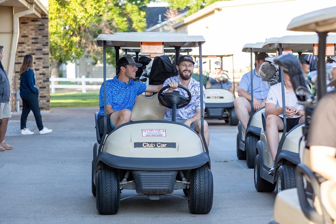 Two men riding in golf cart, similing.