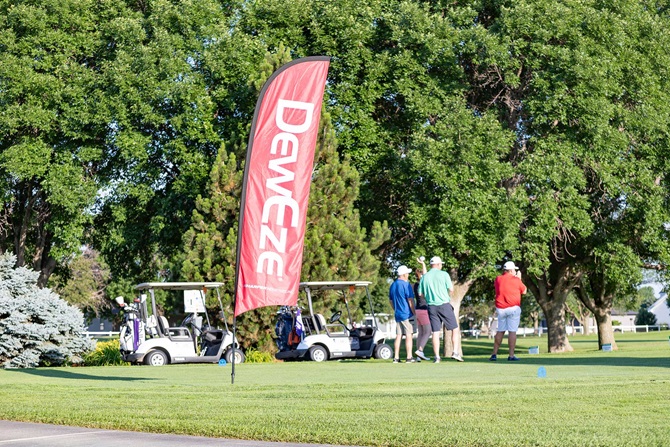 Golfers on greens with large, sponsorship flag stationed at a whole.