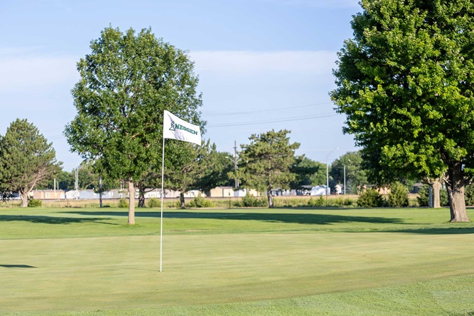 Green golf course with sponsor flag at a hole. 