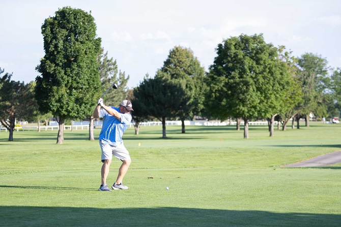 Man swinging at a golf ball on green golf course.