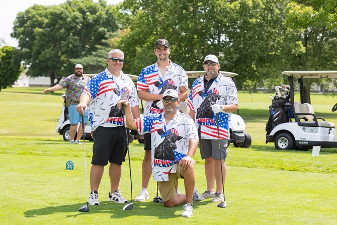 Group of four men on greens at golf course smiling at camera.