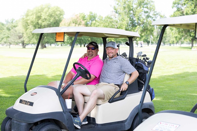 Two men sitting on golf cart at golf course waiting on the next hole.