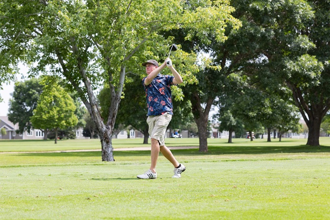 Man swinging golf club at a golf course.