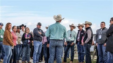 Man in a cowboy hat speaking to a group of people at a sale.