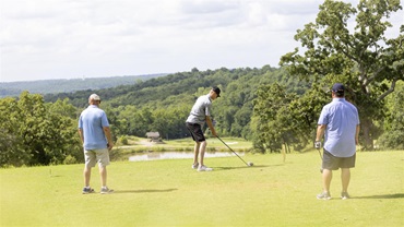 A group of three men playing on a green golf course.