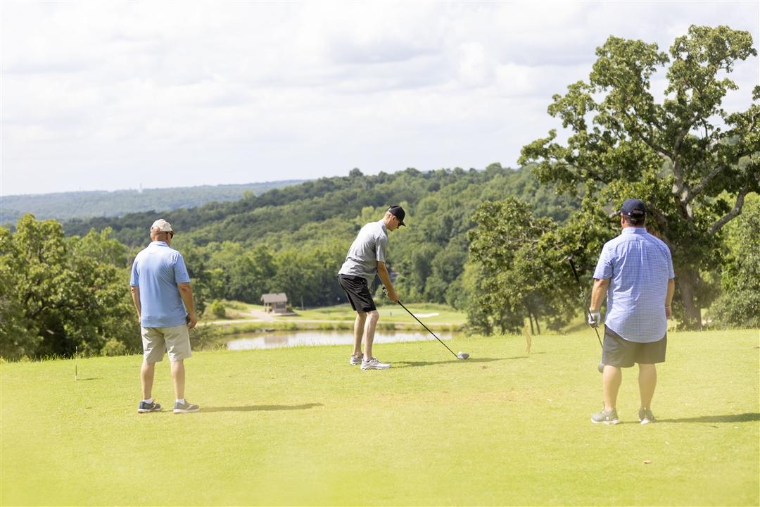 A group of three men playing on a green golf course.