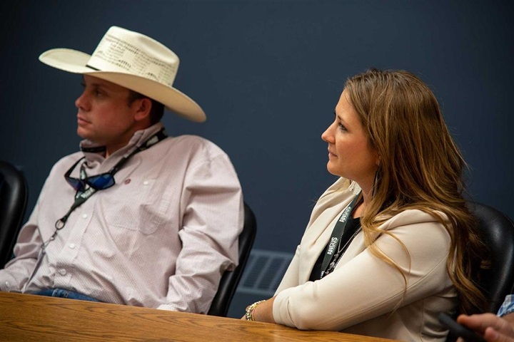 A man and a woman listening to a speaker while sitting at a table.