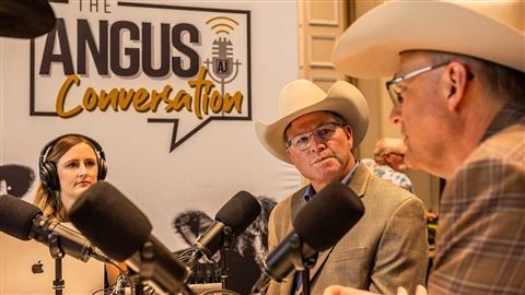 Two men and one woman sit around a table with microphones